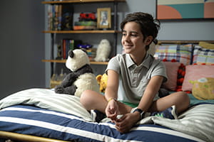 A boy sits on a bed smiling.