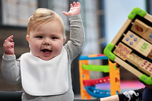 A smiling little boy lifts his hands up while playing with toys.