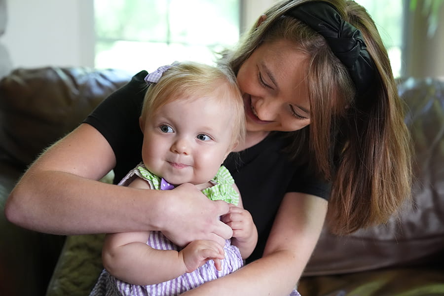 A mom hugs her smiling little girl.