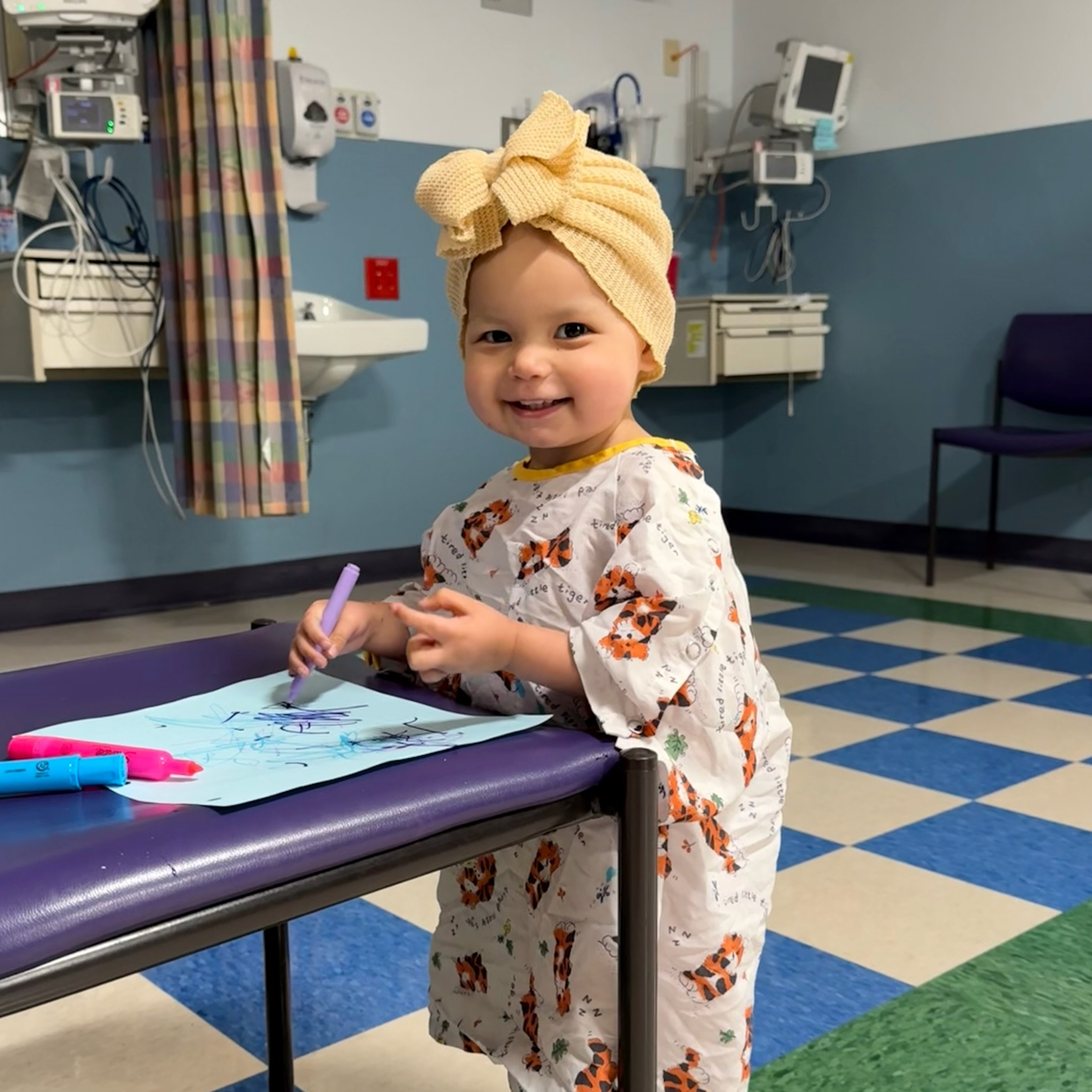 A little girl smiles and colors a picture while at the hospital.