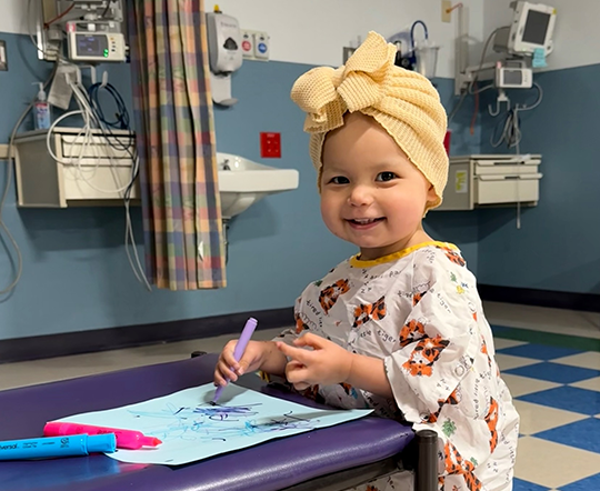 A little girl smiles while coloring at the hospital.