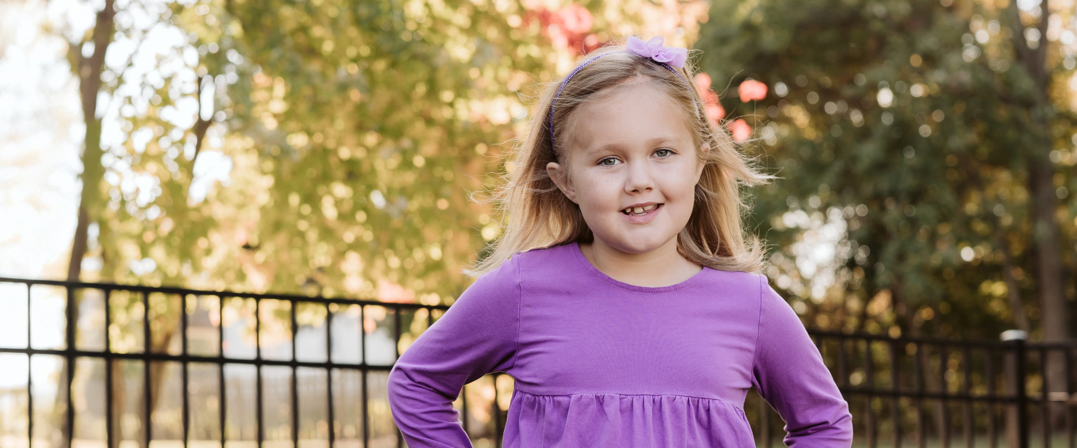 A young girl smiling outside on a sunny day.