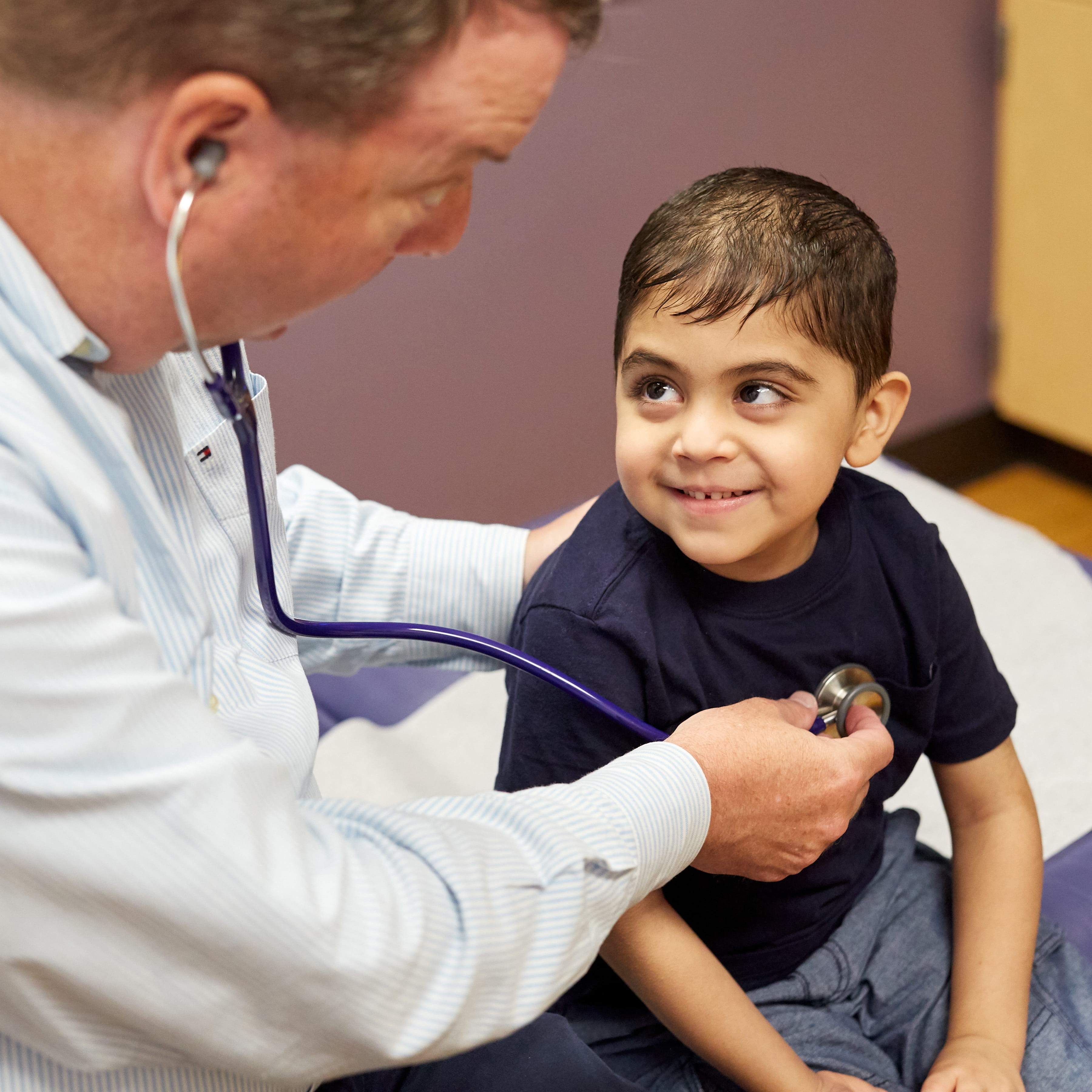 A little boy smiles while a doctor checks his heart rate with a stethoscope. 