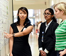 A student presents a research poster to interested onlookers.