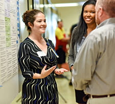 A student presents a research poster to interested onlookers.