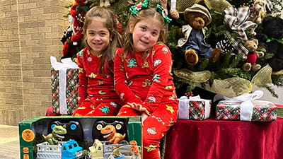Children smiling with gifts by the Christmas tree.