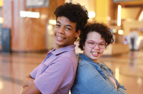 Siblings stand back-to-back.