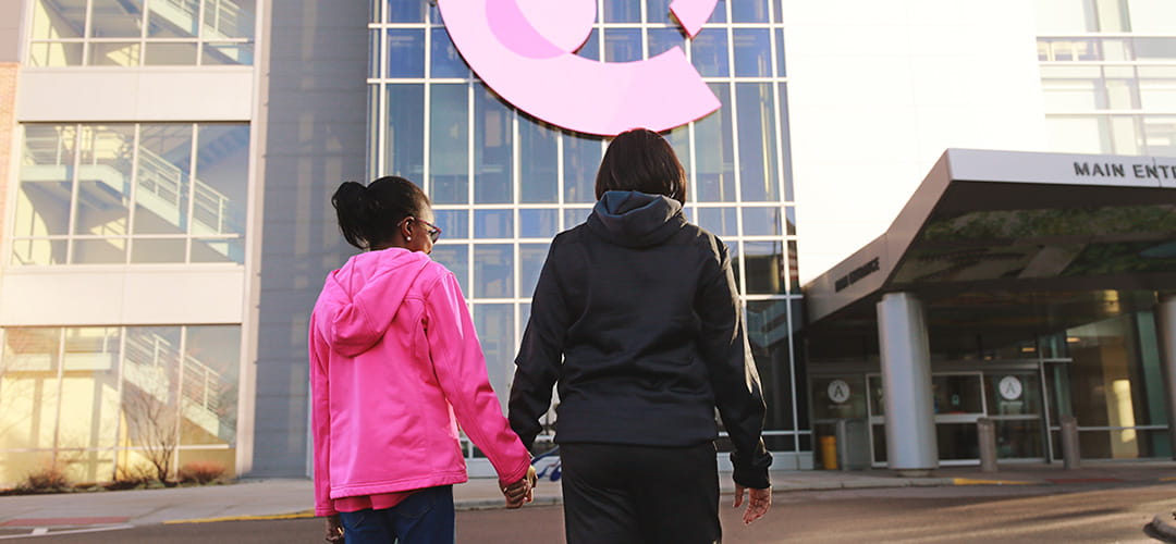 A photo of a mom and daughter holding hands as they walk.