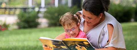 Picture of a mother and daughter reading a book outside.