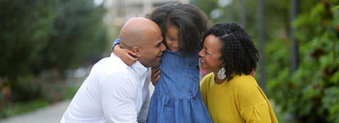 Parents hug their daughter outside.