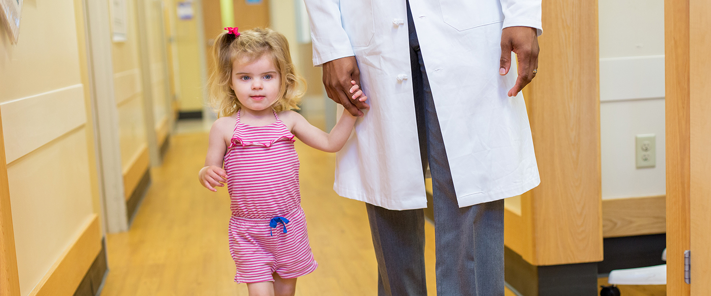 A child walks down a hallway with a doctor.