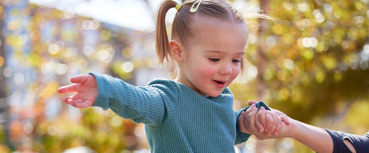 Child playing outside smiling with her parent.