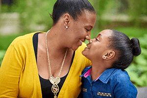 An image of a mom and daughter smiling at each other.