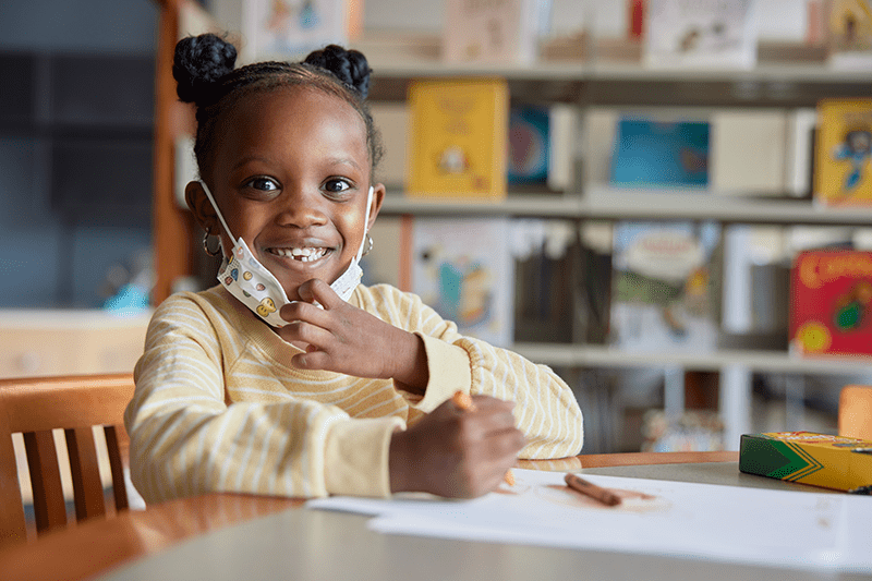 A young girl smiles while coloring.