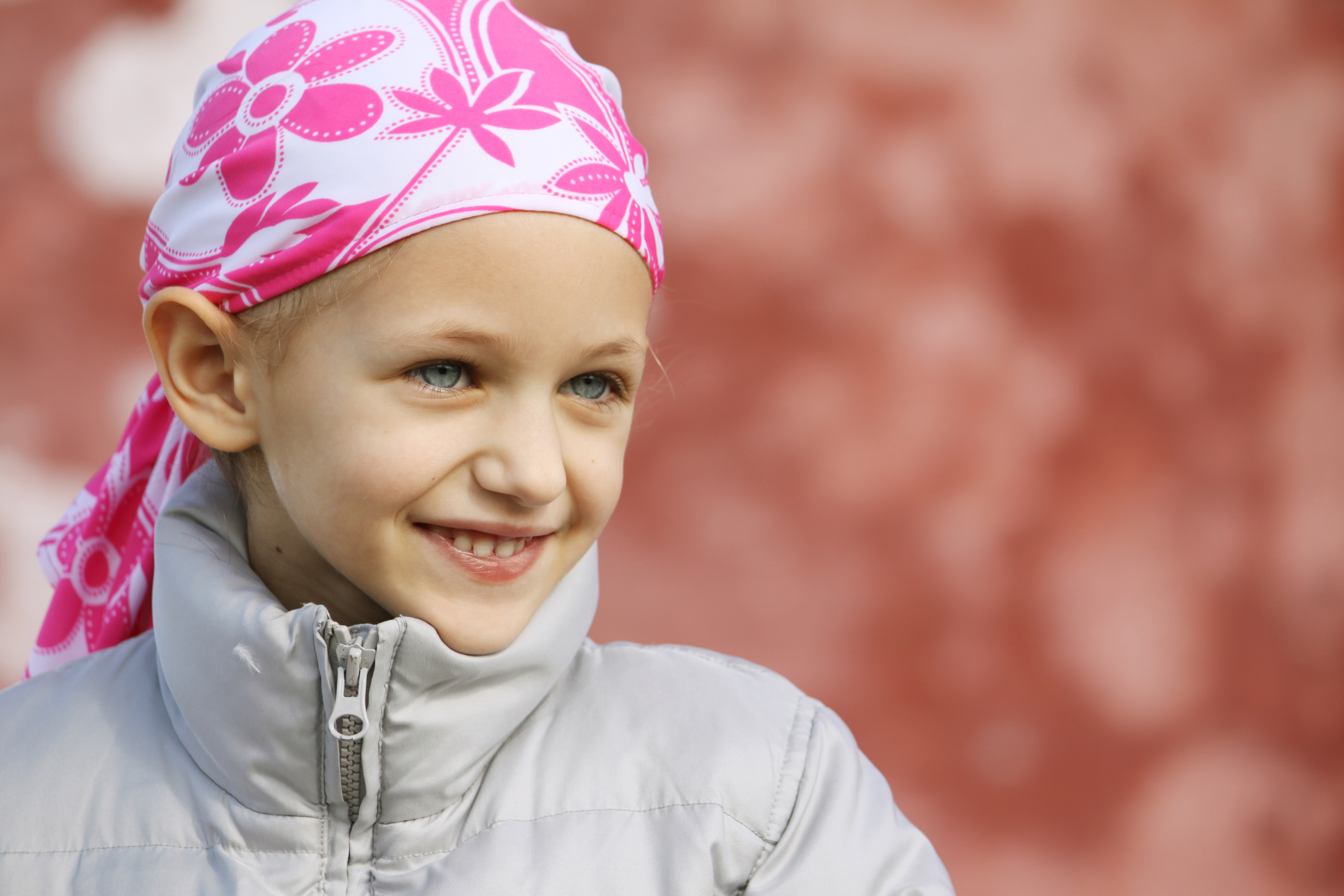 Child with cancer and a scarf on her head smiles.
