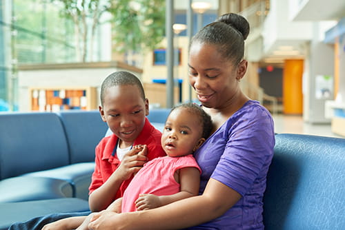 Mother holding infant, and sitting with her older son.