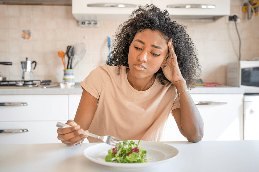 A girl looking confused in front of a plate of food.