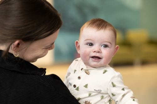 Heart surgery patient, David, smiles at the camera, while mom holds him.