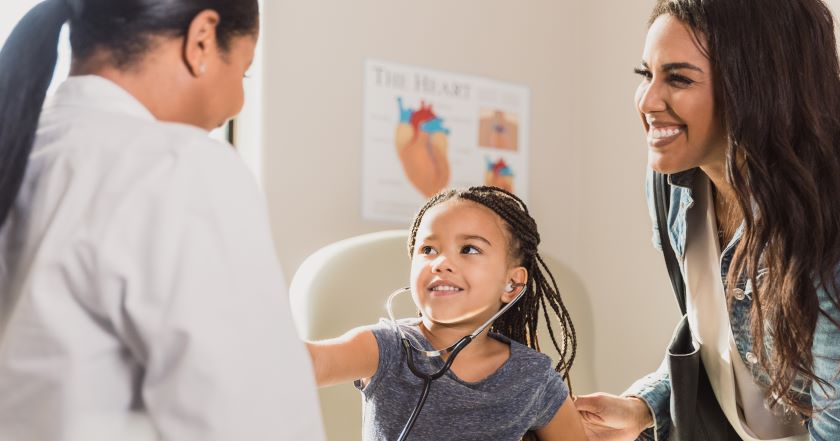 A young patient playfully listens to her doctor's heart with a stethoscope.