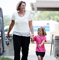 A mother and daughter hold hands while walking.